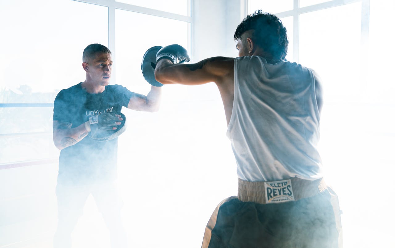 Home Two men engage in a dynamic boxing training session, featuring punching techniques.