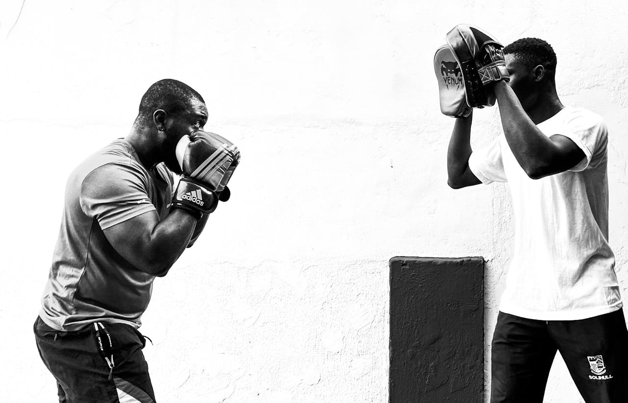 Services Monochrome image of two men training in boxing with focus pads outdoors.