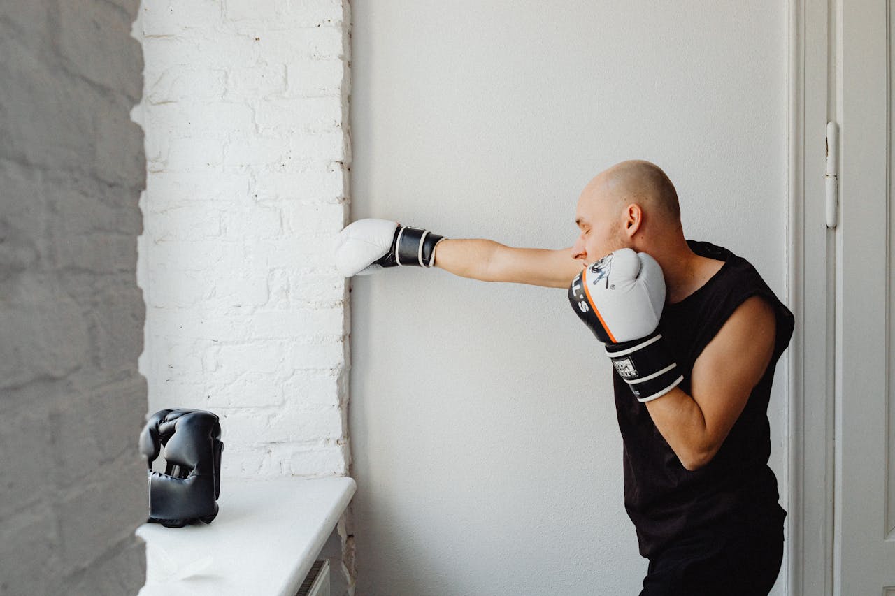 Bald man practices boxing indoors, punching a wall in a training session. Healthy lifestyle concept.